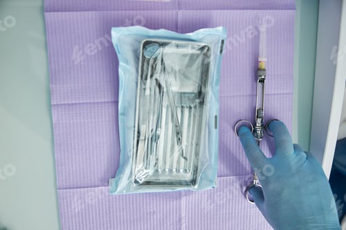 Preview: Hand of medical professional picking syringe near dental instruments