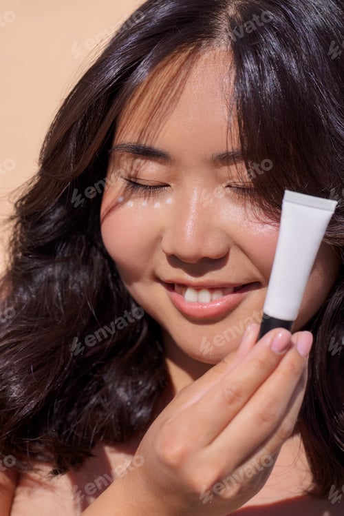 Preview: Asian woman with long dark hair is smiling while holding a skincare product