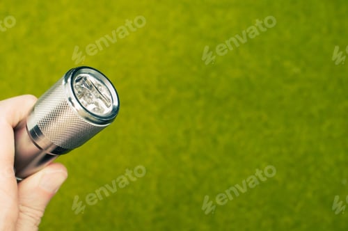 Preview: Selective focus shot of a hand holding a flashlight with green grass on the background