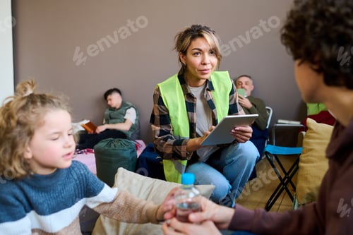Preview: Young female volunteer with tablet sitting on squats in front of woman with son