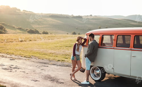 Preview: A young couple on a roadtrip through countryside, standing by minivan.
