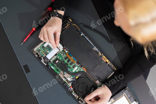 Preview: Female IT technician in her twenties repairing a laptop with tools and open chassis on a workbench