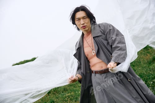 Preview: Stylish young man in grey trench coat enjoying a serene moment in the park