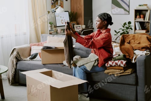 Preview: Black Adult Woman Sorting Clothes for Donation at Home