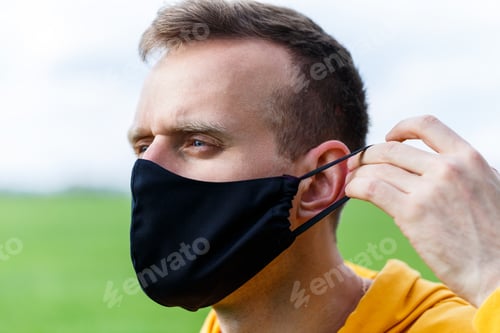 Preview: Young man sitting on green grass in a protective antiviral mask and thinking about the future.