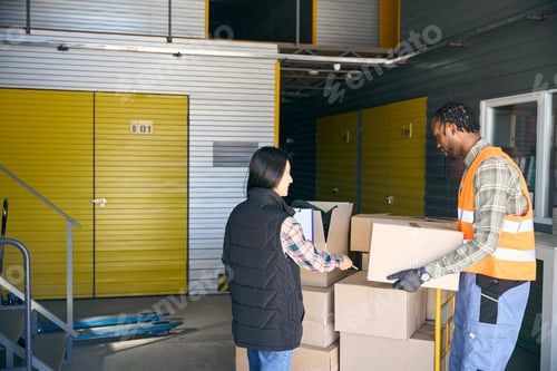 Preview: Freight handler unloading goods supervised by coworker in storehouse