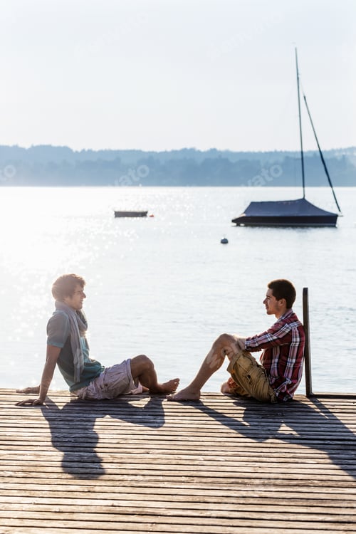 Preview: Friends sitting face to face on wood pier next to lake, Schondorf, Ammersee, Bavaria, Germany