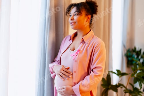 Preview: Pregnant woman showing pink ribbon for breast cancer awareness, looking hopeful