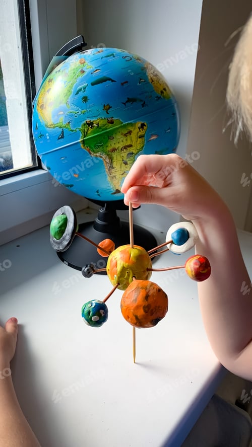 Preview: The child holds in his hands a model of the solar system, which he himself made from plasticine