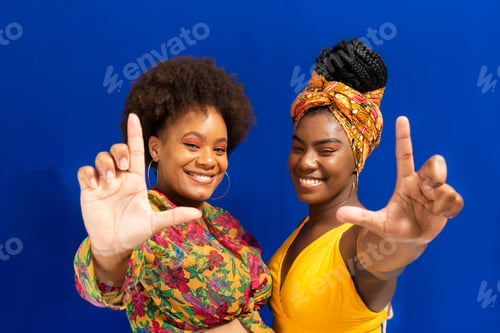 Preview: Portrait of two woman wearing colorful outfits making the v sign for the camera