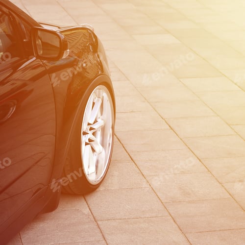 Preview: Diagonal view of a black glossy car with white wheels, which stands on a square of gray tiles