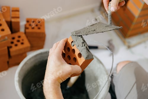 Preview: A young man makes brickwork on the chimney of a fireplace.