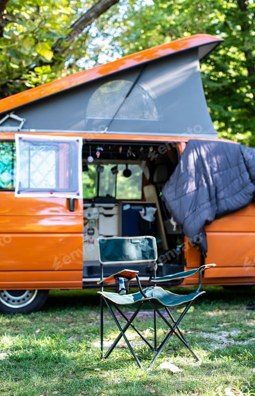 Preview: Camper in campsite. Outdoor equipment and travel van on green me