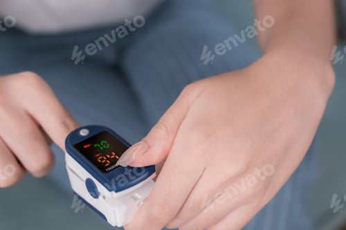 Preview: Asian woman using finger oxygen meter on sofa in living room at home, health and living concept