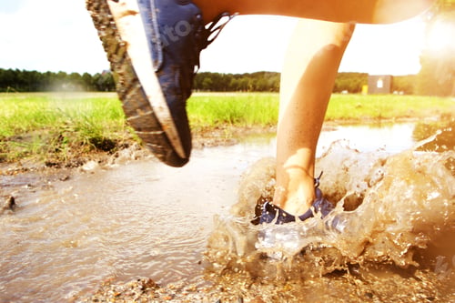 Preview: Runner's sneakers splashing in mud puddle