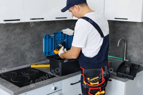Preview: Master in uniform with tools on his belt and a toolbox is ready to assemble furniture in kitchen.