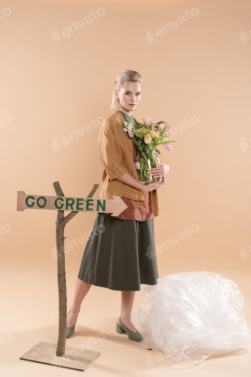 Preview: attractive girl in eco clothing holding vase with flowers near sign with go green lettering on beige