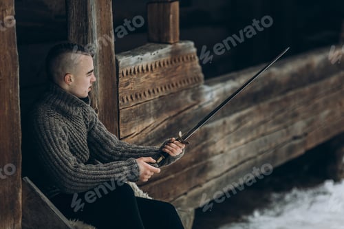 Preview: Portrait of strong viking warrior sharpening his sword, scandinavian viking cosplay