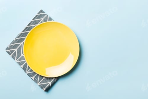 Preview: Top view on colored background empty round yellow plate on tablecloth for food.