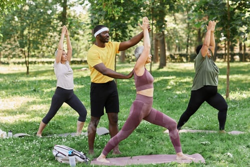 Preview: Sports trainer assisting group of senior women enjoying yoga outdoors in park