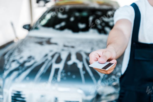 Preview: cropped view of man holding credit card near car with foam