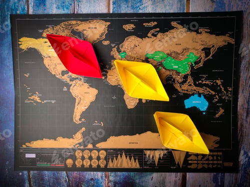 Preview: Colorful paper ships on the world map placed on a wooden table