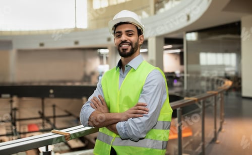 Preview: Happy confident young attractive arabic engineer in hard hat and protective clothing in office plant