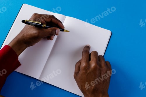 Preview: Hands of biracial man holding pen and writing in notebook with copy space on blue background