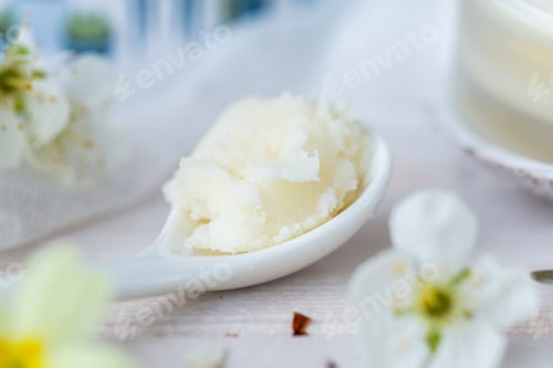 Preview: Selective focus shot of a spoonful of shea butter and some white flowers on a white table top