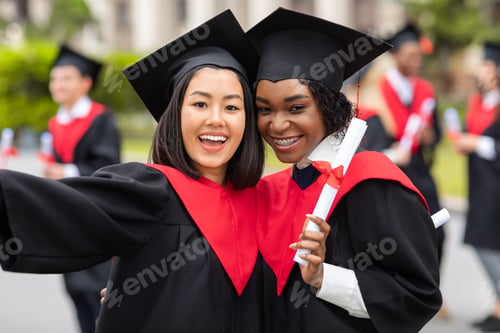 Preview: Cheerful young ladies in graduation robes taking selfie
