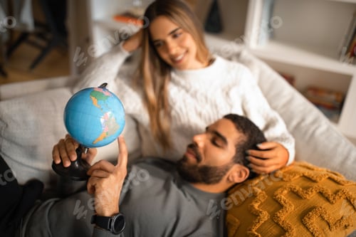 Preview: Smiling millennial european woman and arab male resting in free time, looking at globe, choosing