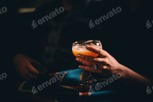 Preview: girl holding a craft cocktail in a hotel bar late at night with a fancy diamond engagement ring