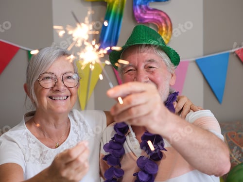 Preview: Two smiling caucasian seniors celebrating at home 75th birthday with sparkles