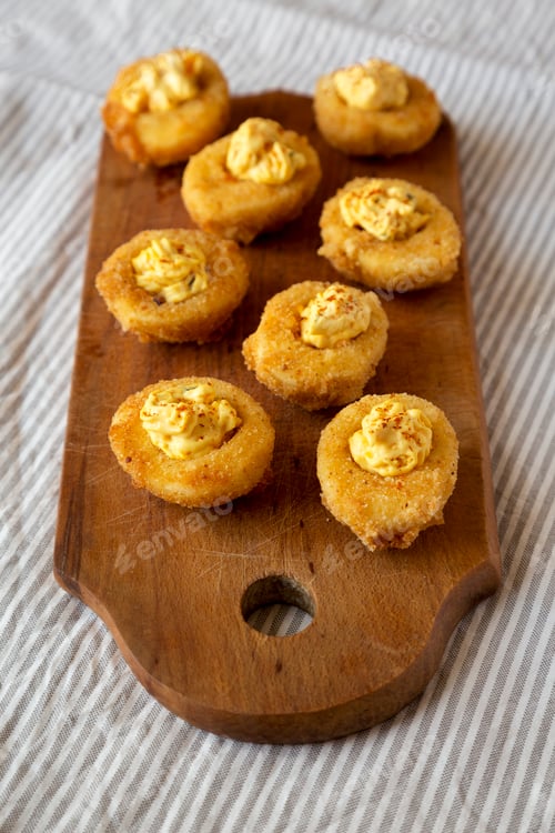 Preview: Homemade Deep-fried Deviled Eggs with Paprika on a rustic wooden board, low angle view.