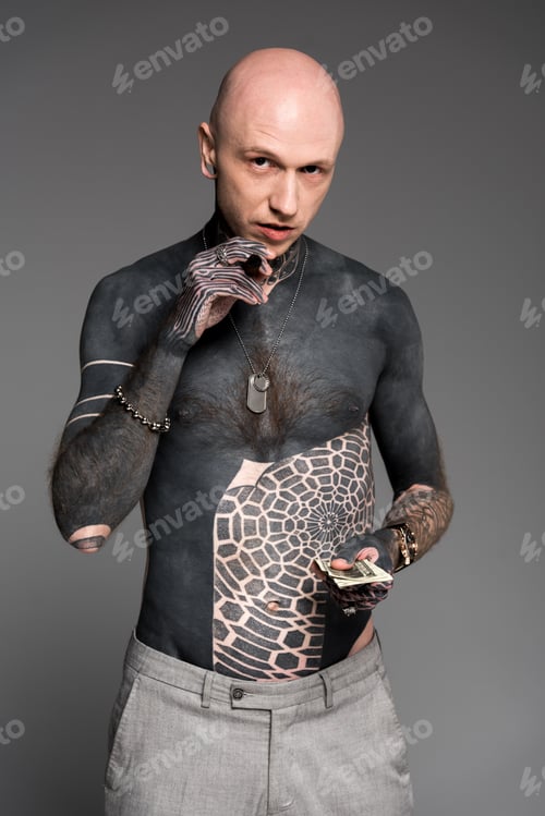 Preview: bald shirtless tattooed man with cigar holding dollar banknotes and looking at camera isolated on