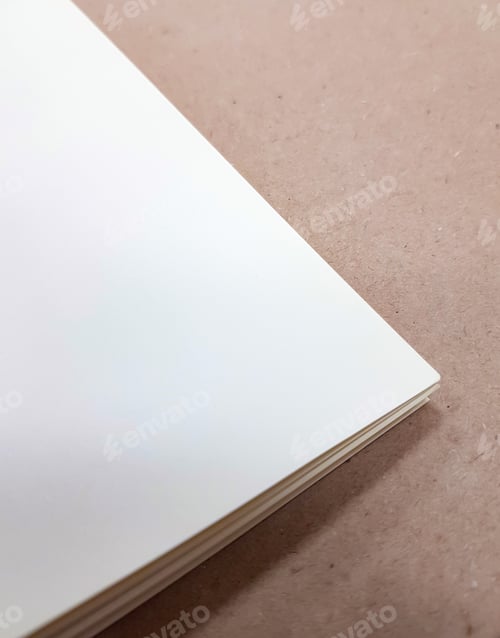 Preview: A corner of a stack of white paper sheets lies on a brown background. Space for text. Top view