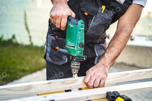 Preview: Unrecognizable male carpenter using electric drill on a wooden plank outdoors
