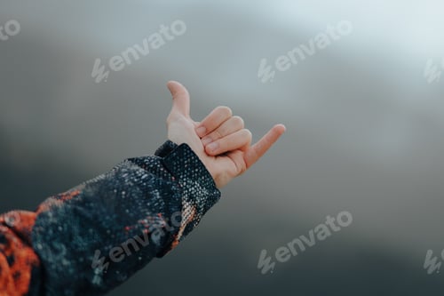 Preview: Unrecognizable male hand wearing a coat making the hang loose sign