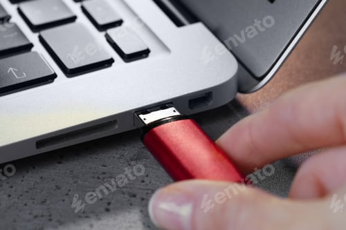 Preview: Woman attaching usb flash drive into laptop at light grey table, closeup