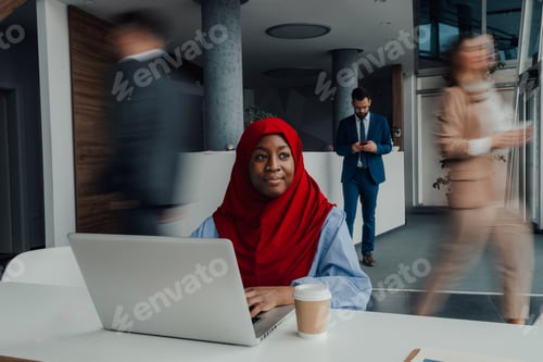 Preview: Focused muslim businesswoman working on laptop in busy office