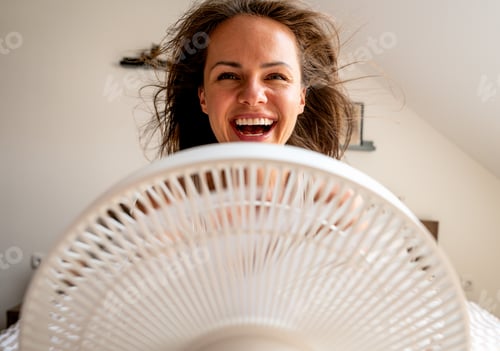 Preview: Laughing woman cooling down in front of fan with wind blowing through her hair