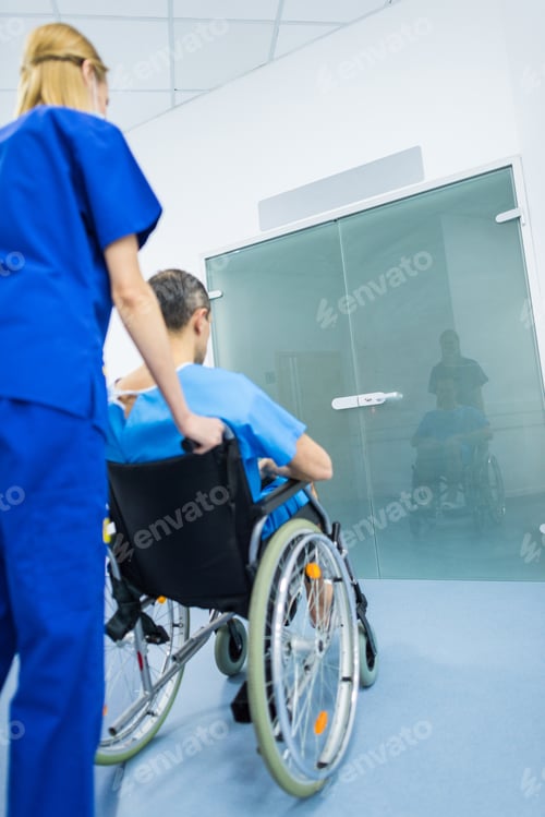 Preview: back view of surgeon and male patient in wheelchair in hospital corridor
