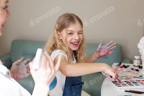Preview: Funny cute girl laughs and gets dirty paints her hands, plays with her mother