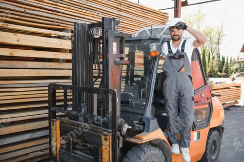 Preview: Warehouse worker posing on forklift near lumber stacks