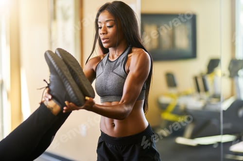 Preview: personal trainer helping woman stretch in gym