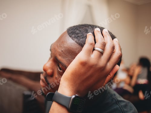 Preview: Black father at home looking sad or worried while family plays happily in the background
