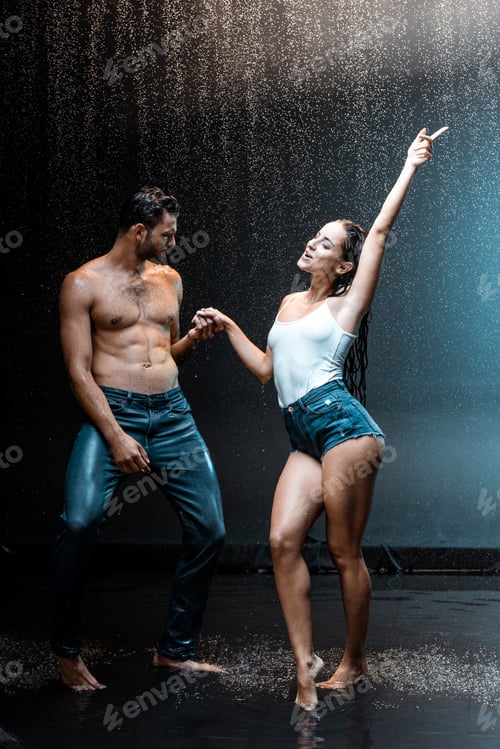 Preview: cheerful couple standing and holding hands under raindrops on black