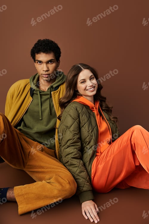 Preview: A fashionable young couple in vibrant autumn outfits sitting together indoors