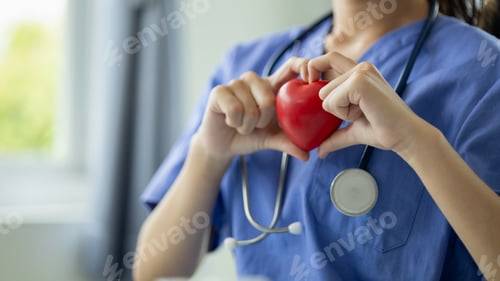 Preview: Beautiful young woman doctor in medical uniform holding a small fake heart, medical professional and