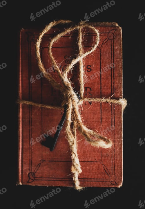 Preview: Top view of vintage red poem book with a key tied with a rope on black background